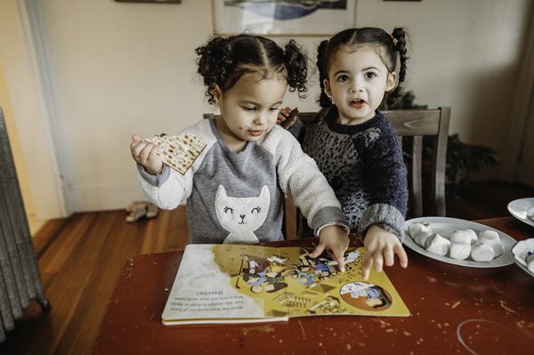 Twin sisters enjoy a snack while reading a PJ Library book