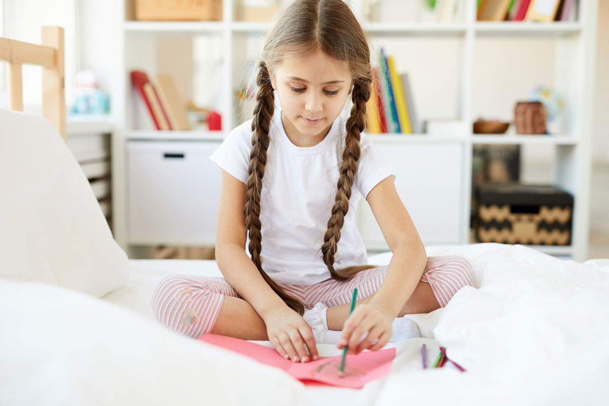 Girl coloring with color pencils on her bed