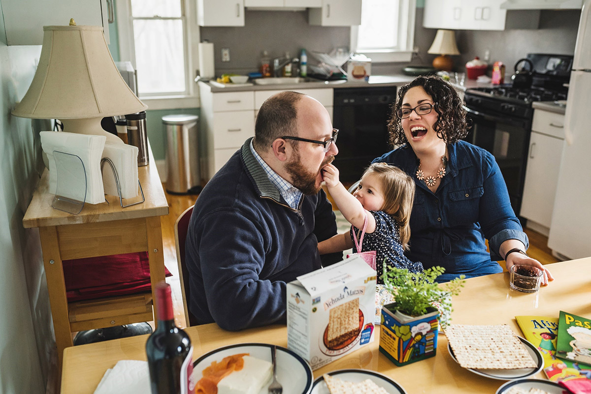 girl feeds matzah to dad as mom looks on