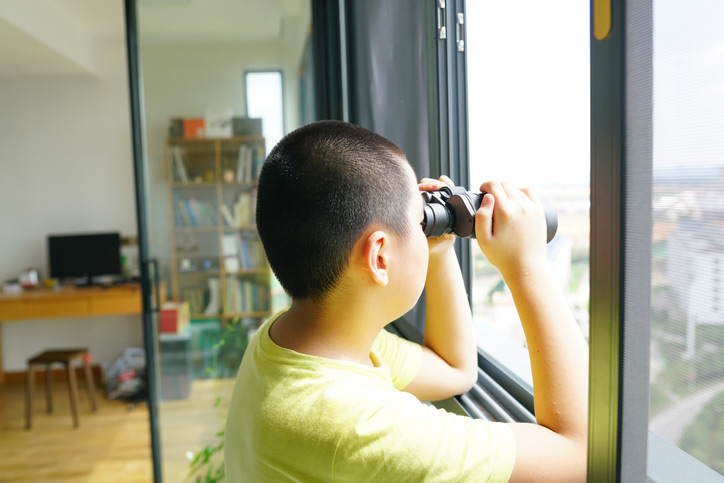 A kid looking out the window with binoculars