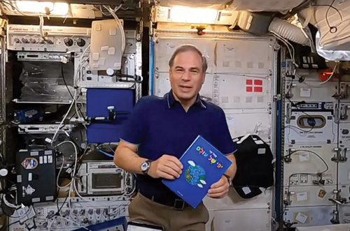 An astronaut holding up the book, A Beautiful World on the International Space Station