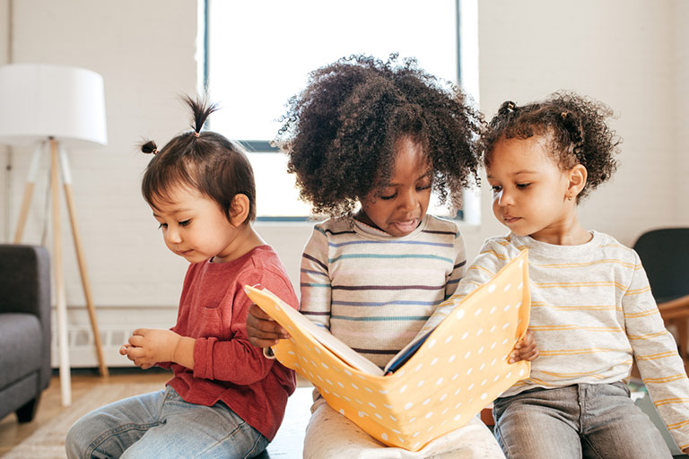 Three young children looking at a book with a yellow Polka Dot cover.