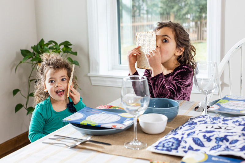 Two girls playing with and eating matzah at a set Passover table.