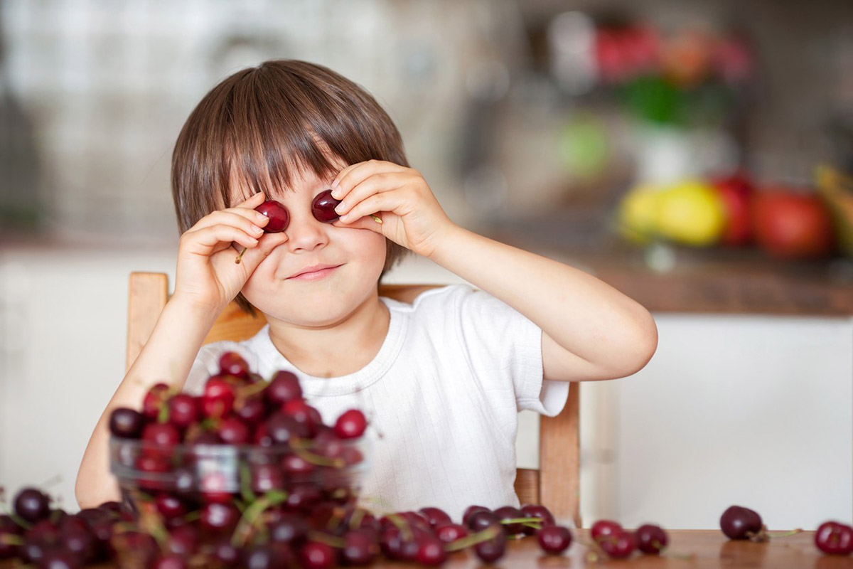 Child holding cherries up to eyes