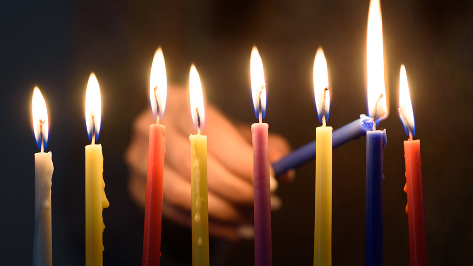 A colorful array of menorah candles being lit in a dark background