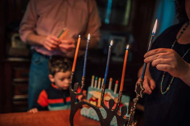 A woman holding a lit candle and placing it into a menorah