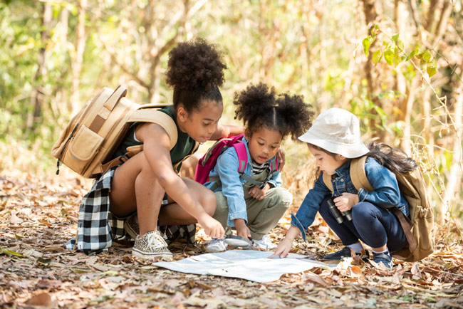 Three children looking at a map on the forest floor