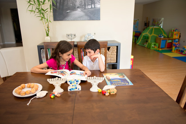 Two children sitting at a table filled with Hanukkah items, smiling at each other