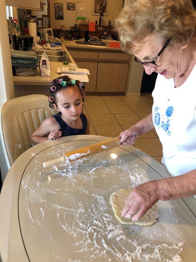 A grandmother prepares the dough for apple crisp while grandchild watches.