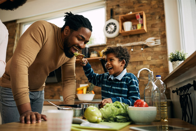 A father and son smile while sharing salad