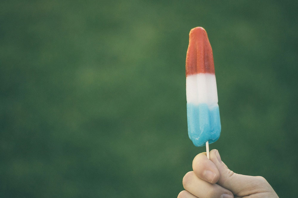 a hand holding a red, white and blue popsicle