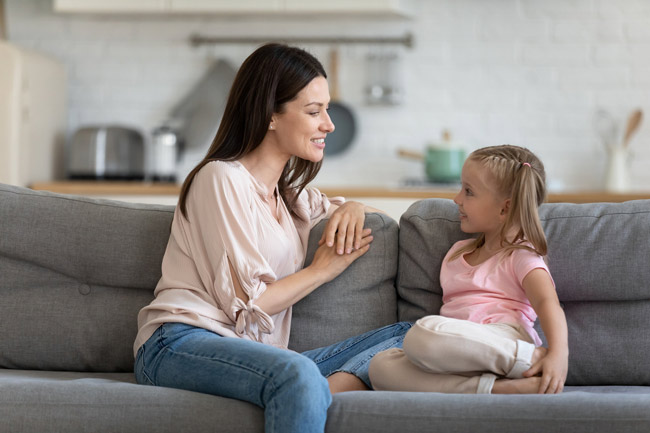 A mother and daughter sitting on a couch talking to each other