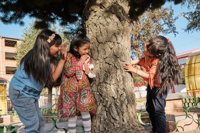 Three latina girls playing around a tree.