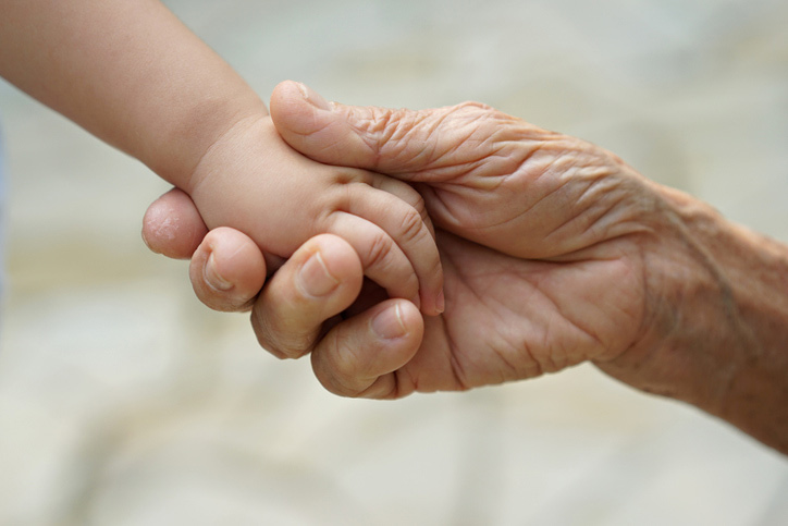 A young babies hands holding hands with an older person's hands