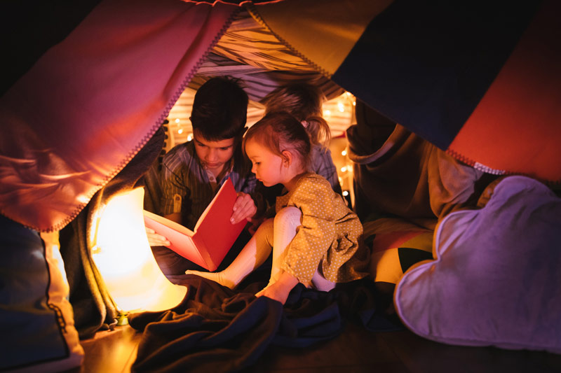 Two children reading a book under blanket fort