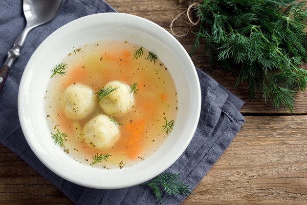 Bowl of matzo ball soup with a bunch of dill on the table