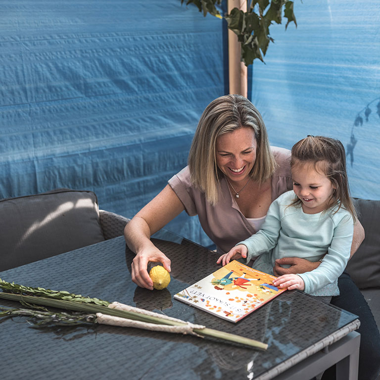 Parent and child in a sukkah reading a book together