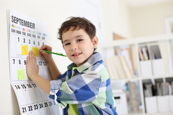 A little boy adds post it notes to a wall calendar