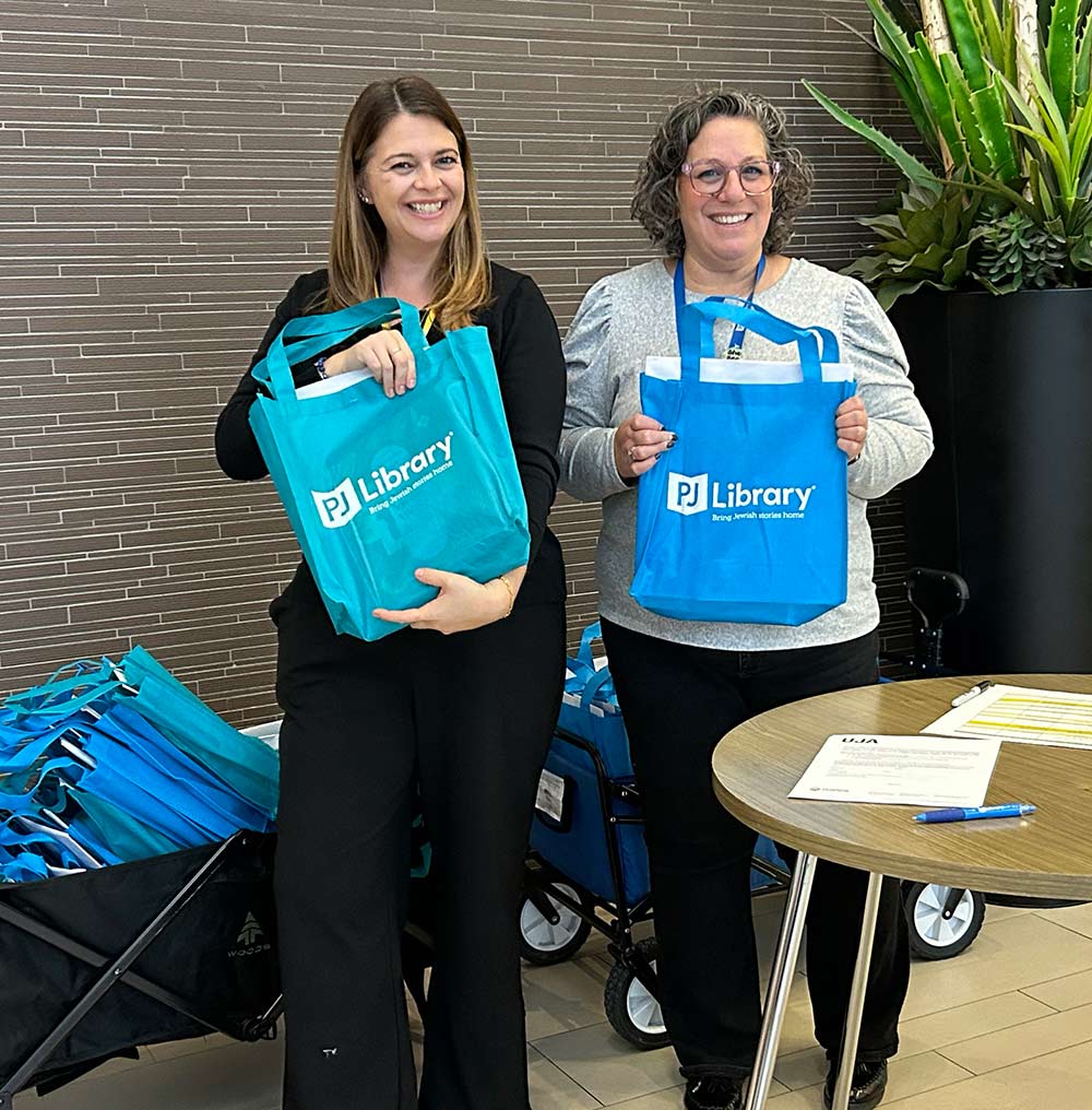 Sam and Jenna holding PJ Library bags
                        