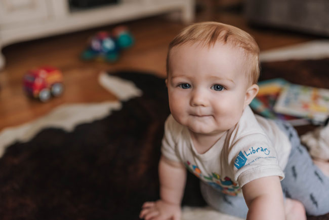 A baby on the floor wearing a PJ Library shirt