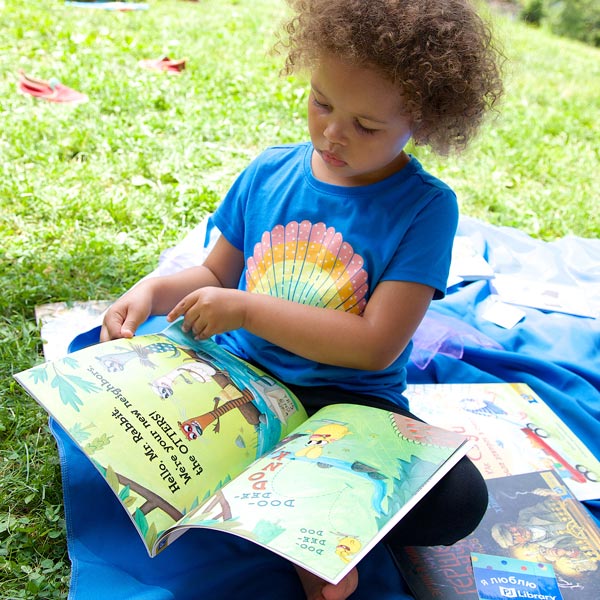 A child sits outside on a blanket reading a book