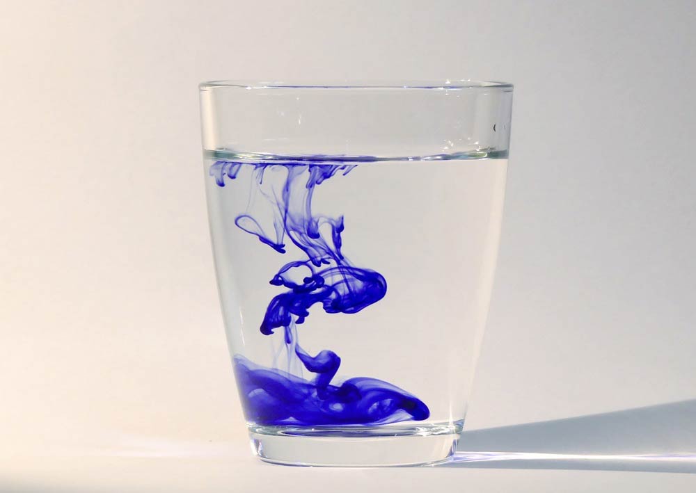 Image of a cup of water with blue food color dissolving into it