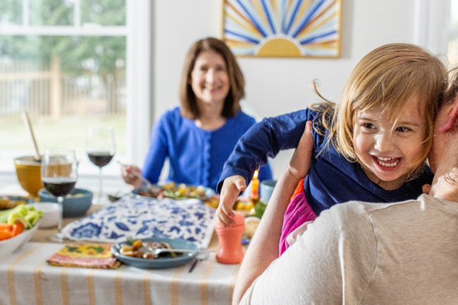 A smiling child being held, with a dinner table full of food in the background