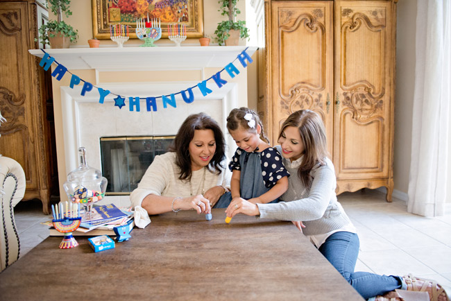 Two women and a little girl at a table playing with dreidels