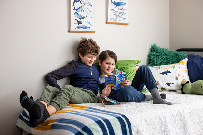 Two kids laying on a bed reading a book