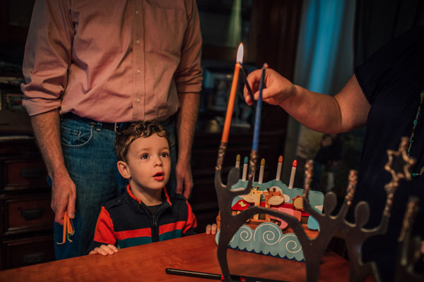 A boy watches intently as a candle on a menorah is lit