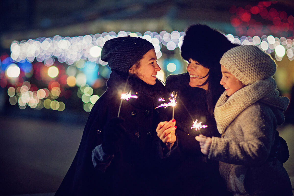 woman with two girls in winter jackets and hats holding sparklers